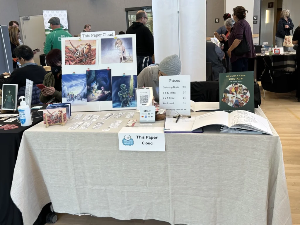 A table of Theresa Arzola's work under the brand This Paper Cloud, showcasing a coloring book, prints, and colorable bookmarks